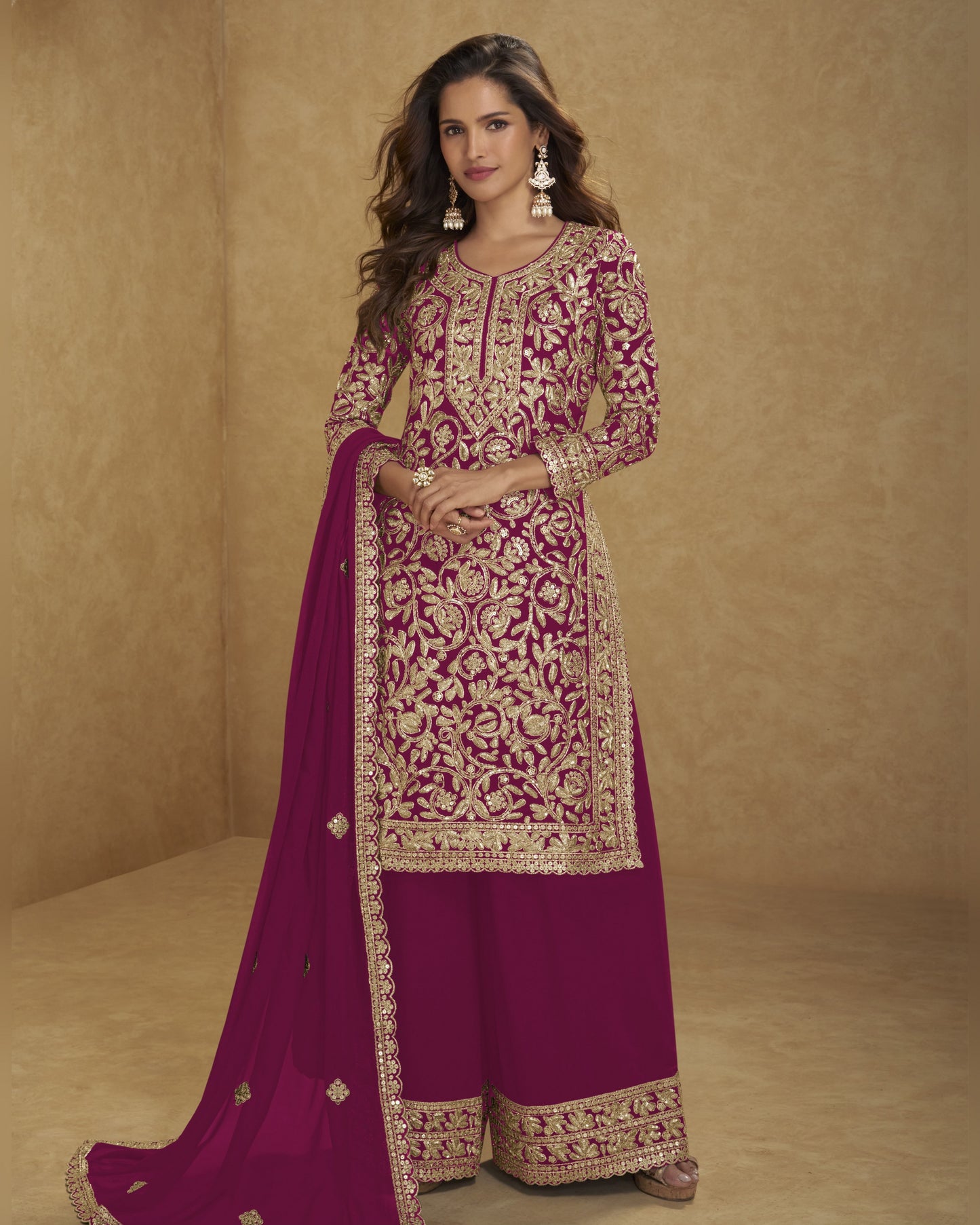 Woman wearing a traditional embroidered outfit with a pink dupatta on a beige background
