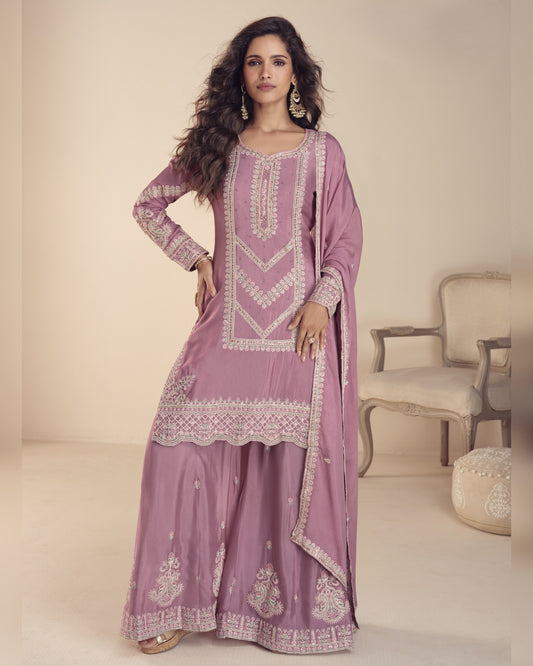 Woman wearing a mauve traditional outfit with white embroidery in a minimalistic setting.