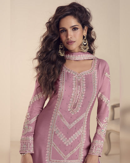 Woman wearing a pink embroidered traditional outfit with a neutral background