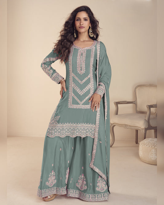 Woman wearing a light blue embroidered traditional outfit in a minimalistic setting.