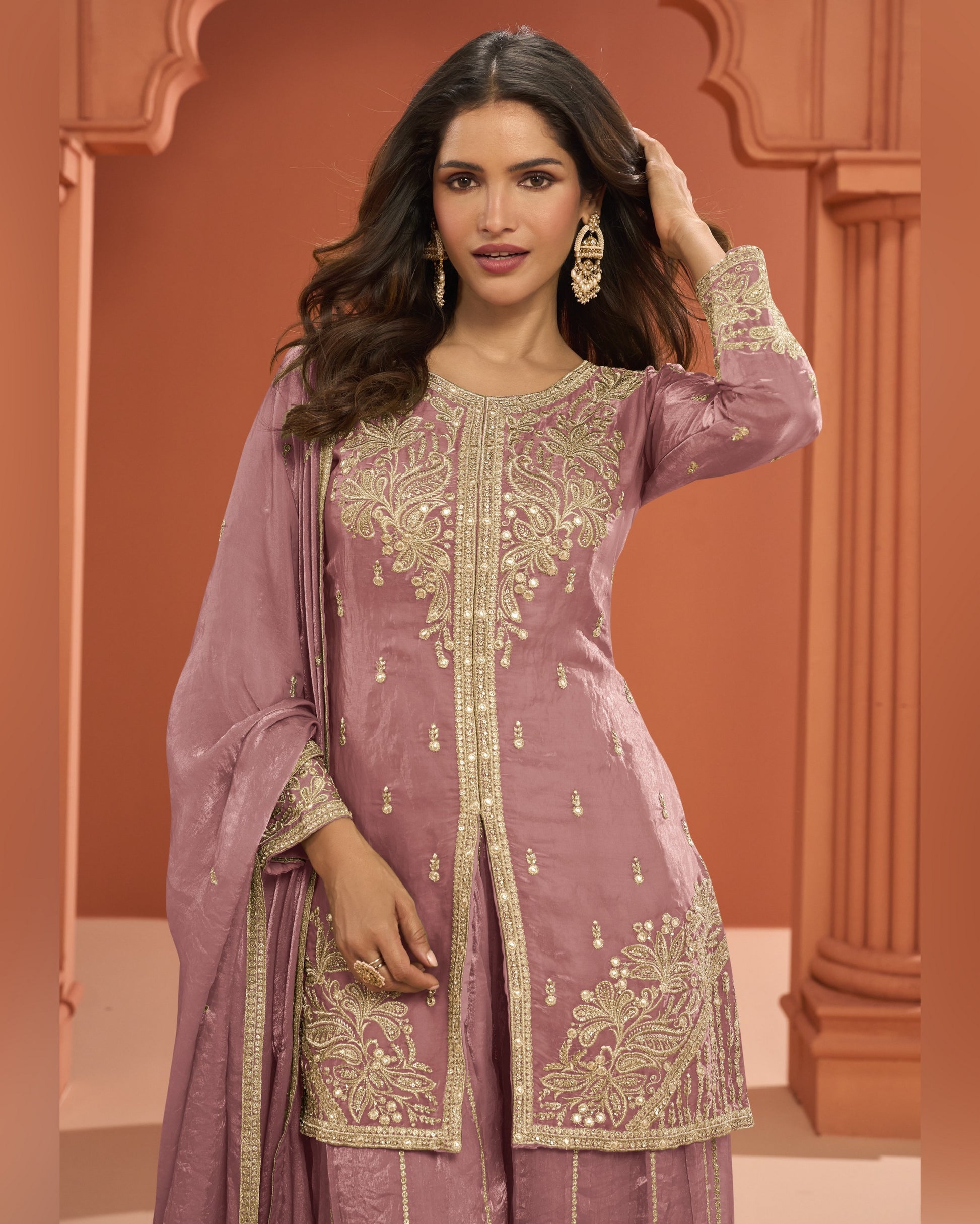 Woman wearing a mauve embroidered traditional outfit with gold details against a warm-toned background.