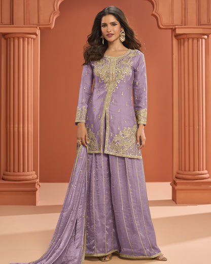 Woman wearing a traditional lavender outfit with gold embroidery against an architectural background.