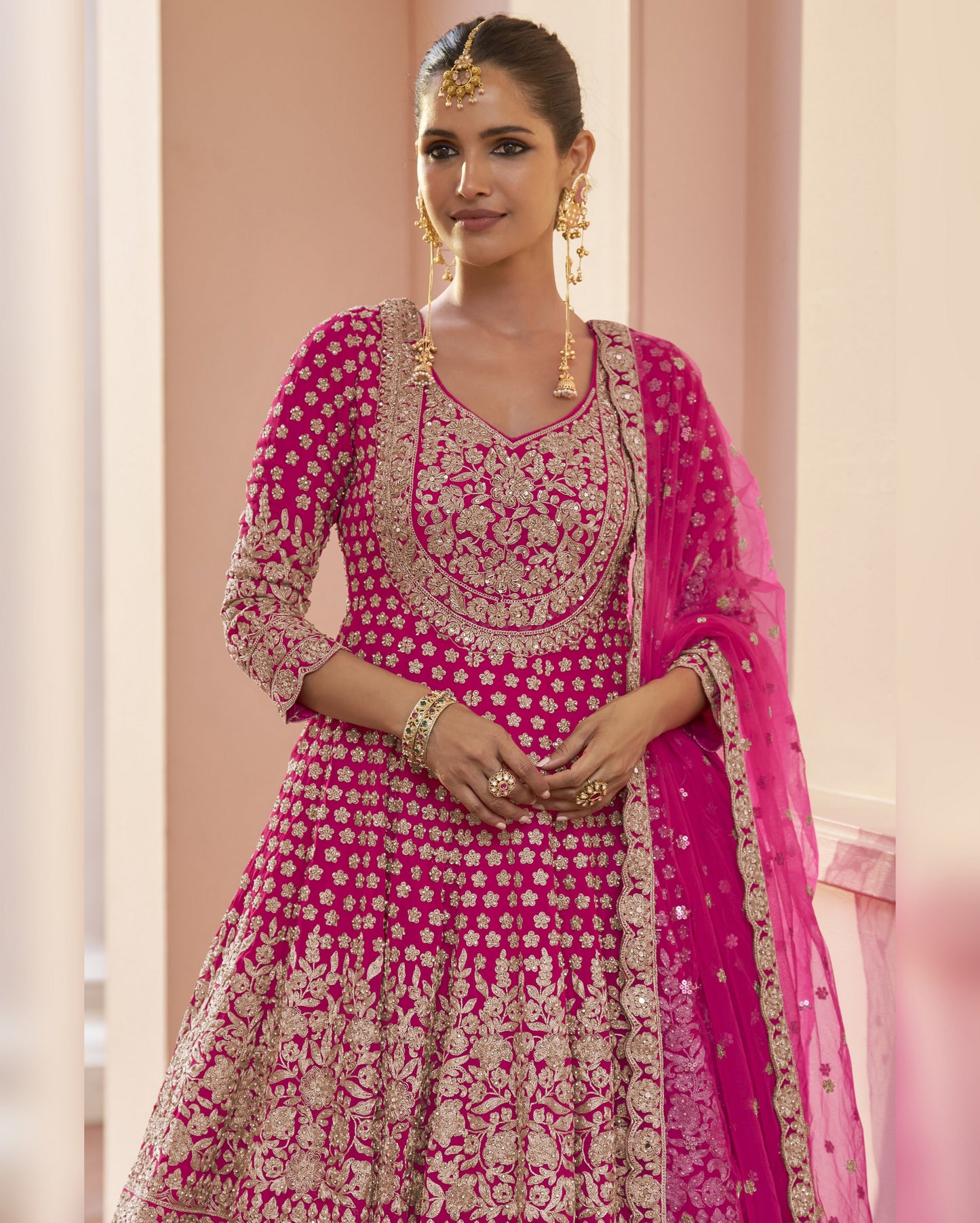 Woman wearing a pink and gold embroidered traditional outfit with a dupatta.