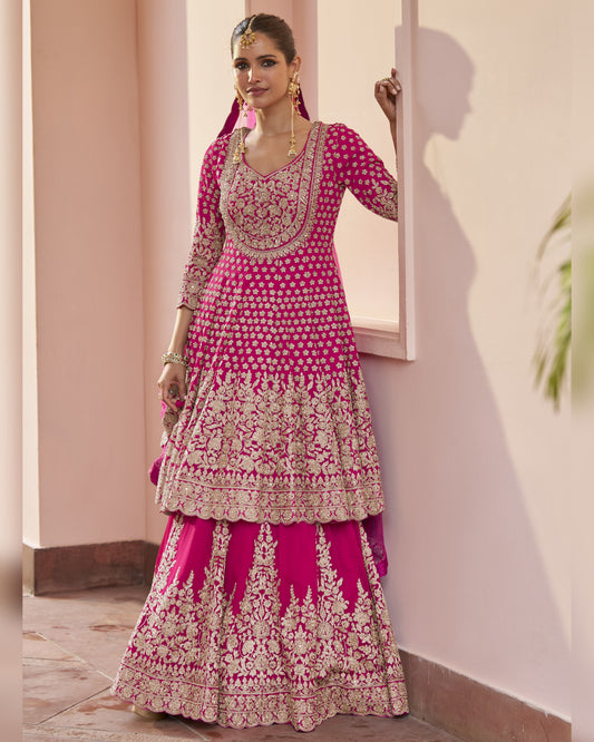 Woman wearing a pink and gold embroidered traditional outfit indoors.