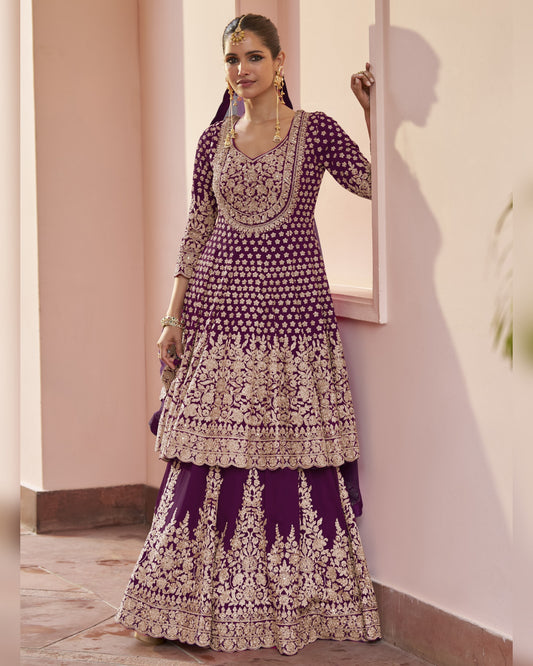 Woman wearing a traditional purple and white embroidered outfit against a light pink wall.