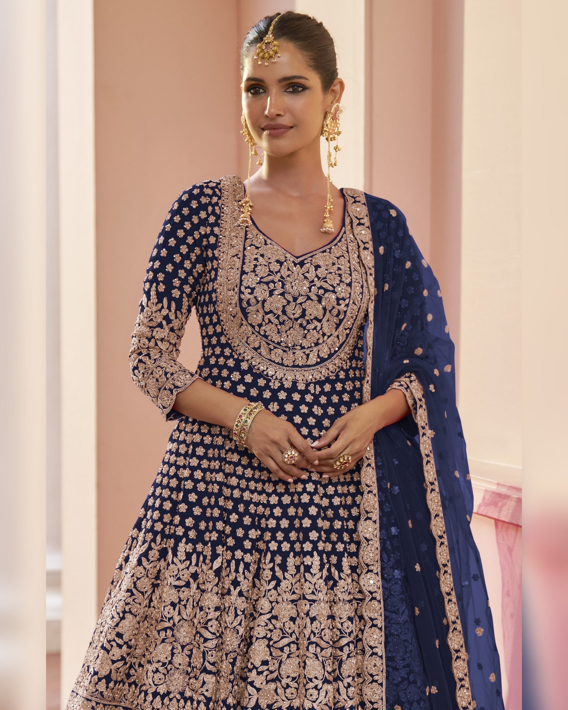 Woman wearing a traditional embroidered outfit with a blue dupatta against a light pink background