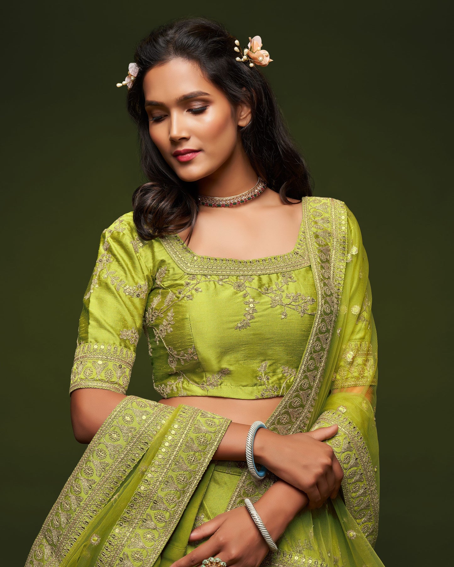 Woman wearing a green traditional outfit with intricate designs on a dark background