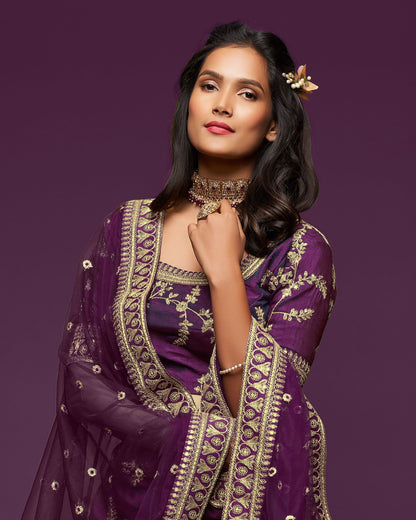 Woman wearing a purple embroidered traditional outfit against a purple background