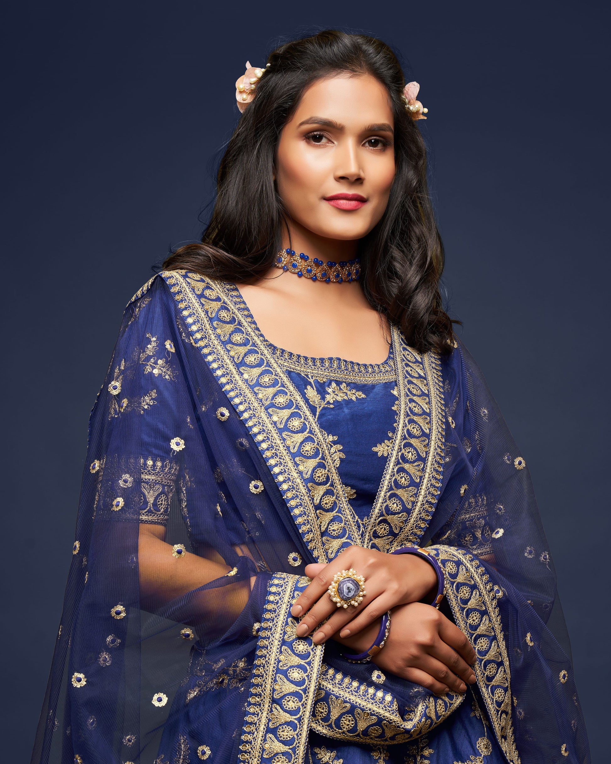 Woman wearing a blue embroidered traditional outfit against a dark background