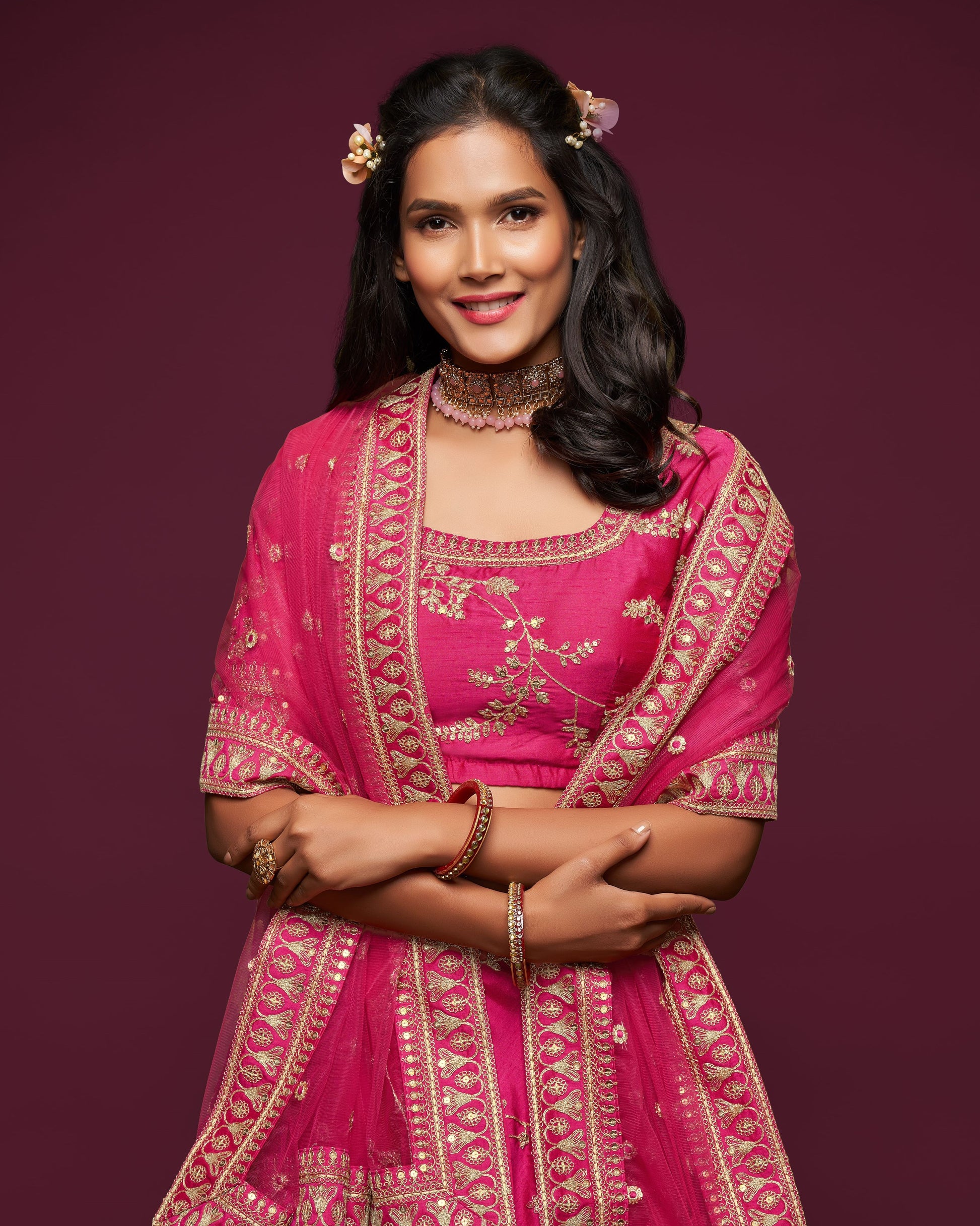 Woman wearing a pink traditional outfit with gold embroidery on a dark purple background