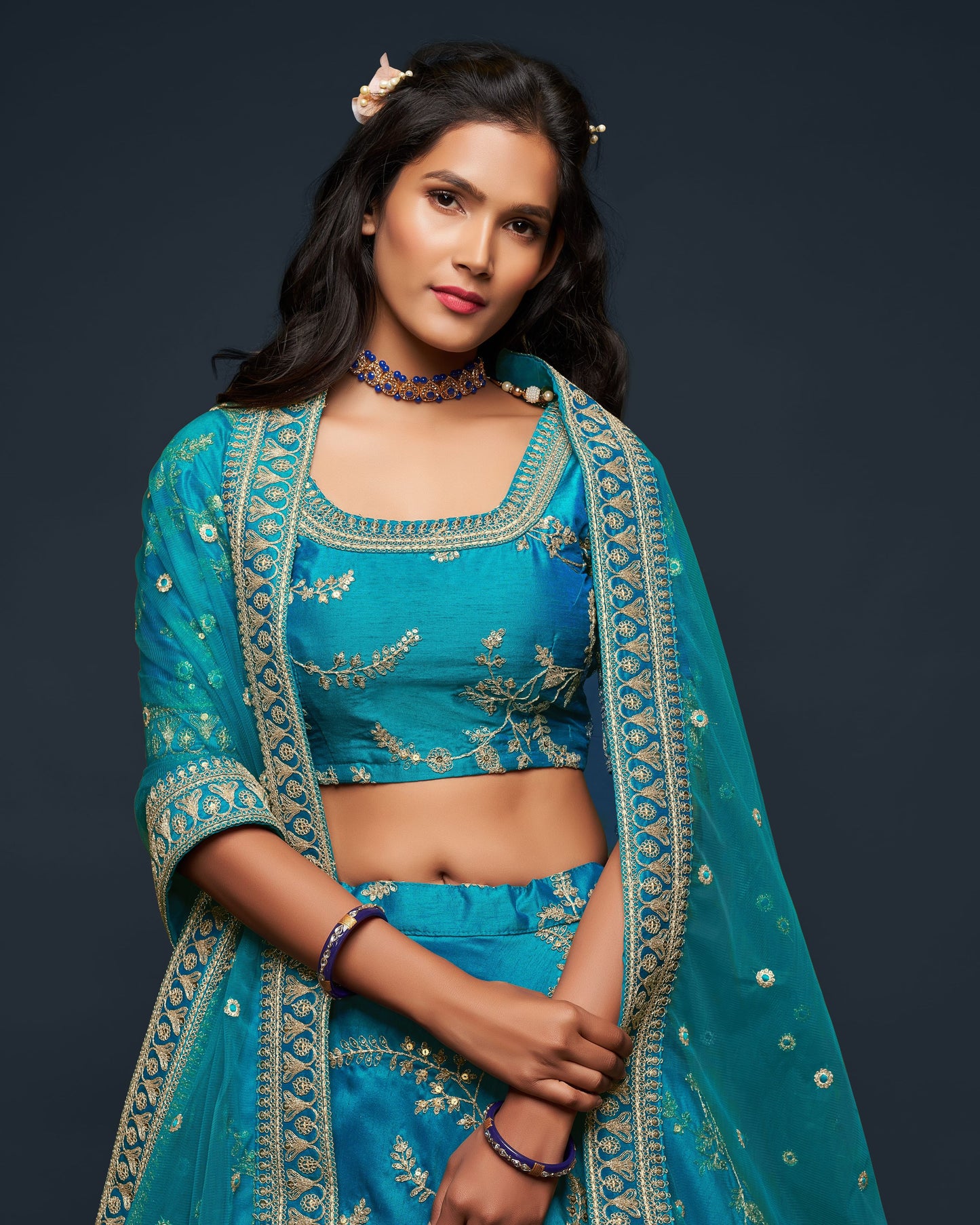 Woman wearing a traditional blue embroidered outfit against a dark background