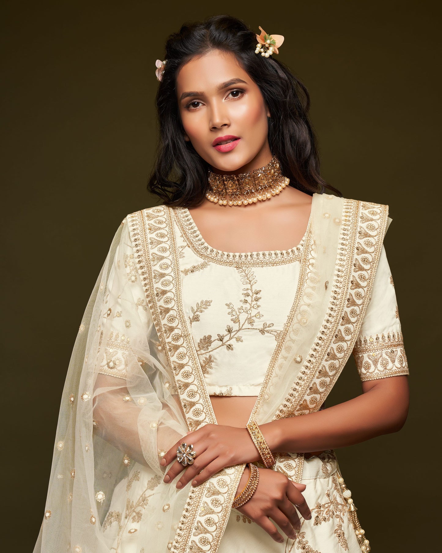 Woman wearing a traditional embroidered outfit with gold jewelry against a dark background