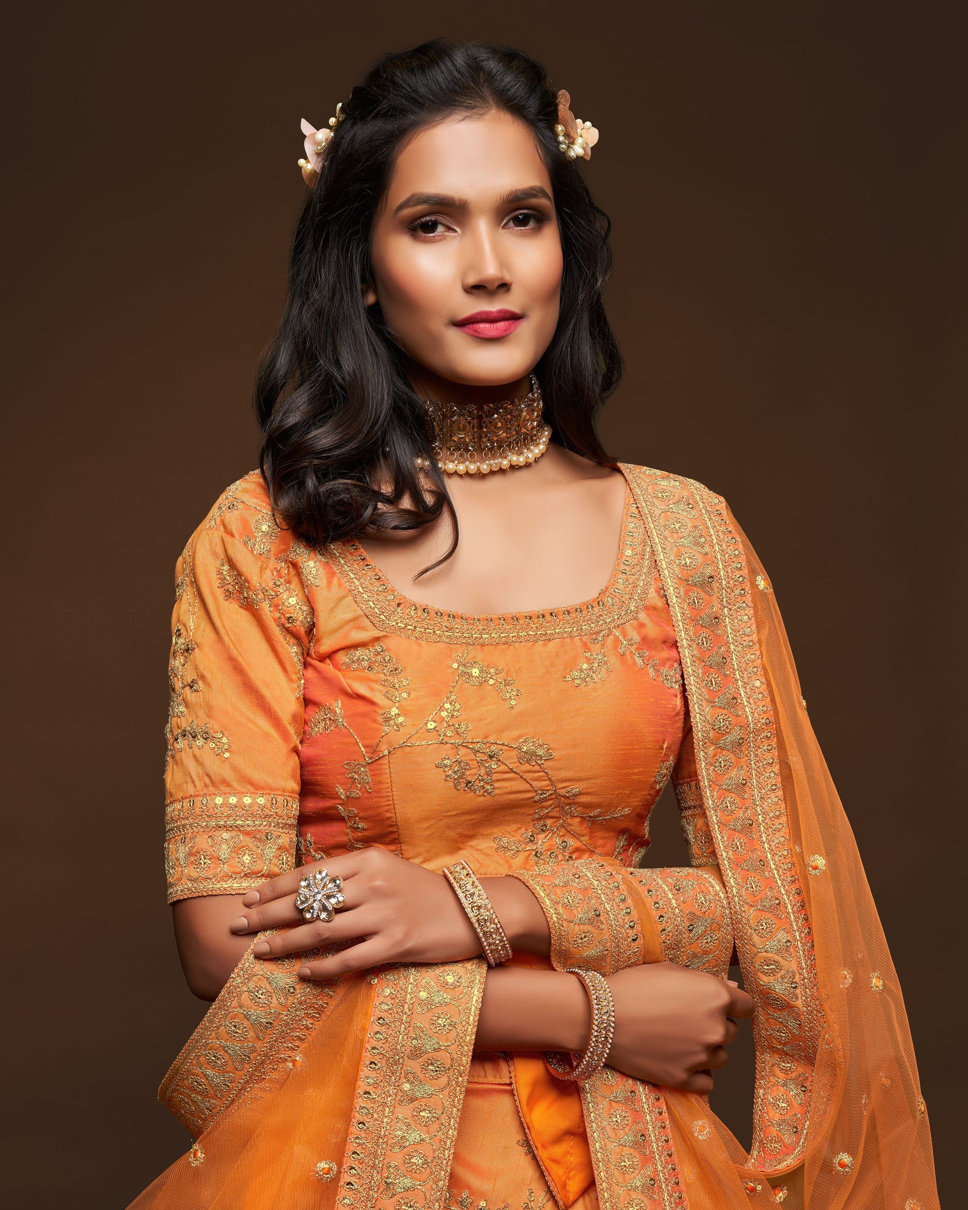 Woman wearing an orange traditional outfit with intricate designs on a brown background