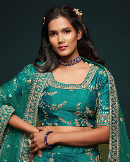 Woman wearing a traditional teal embroidered outfit with a dark background