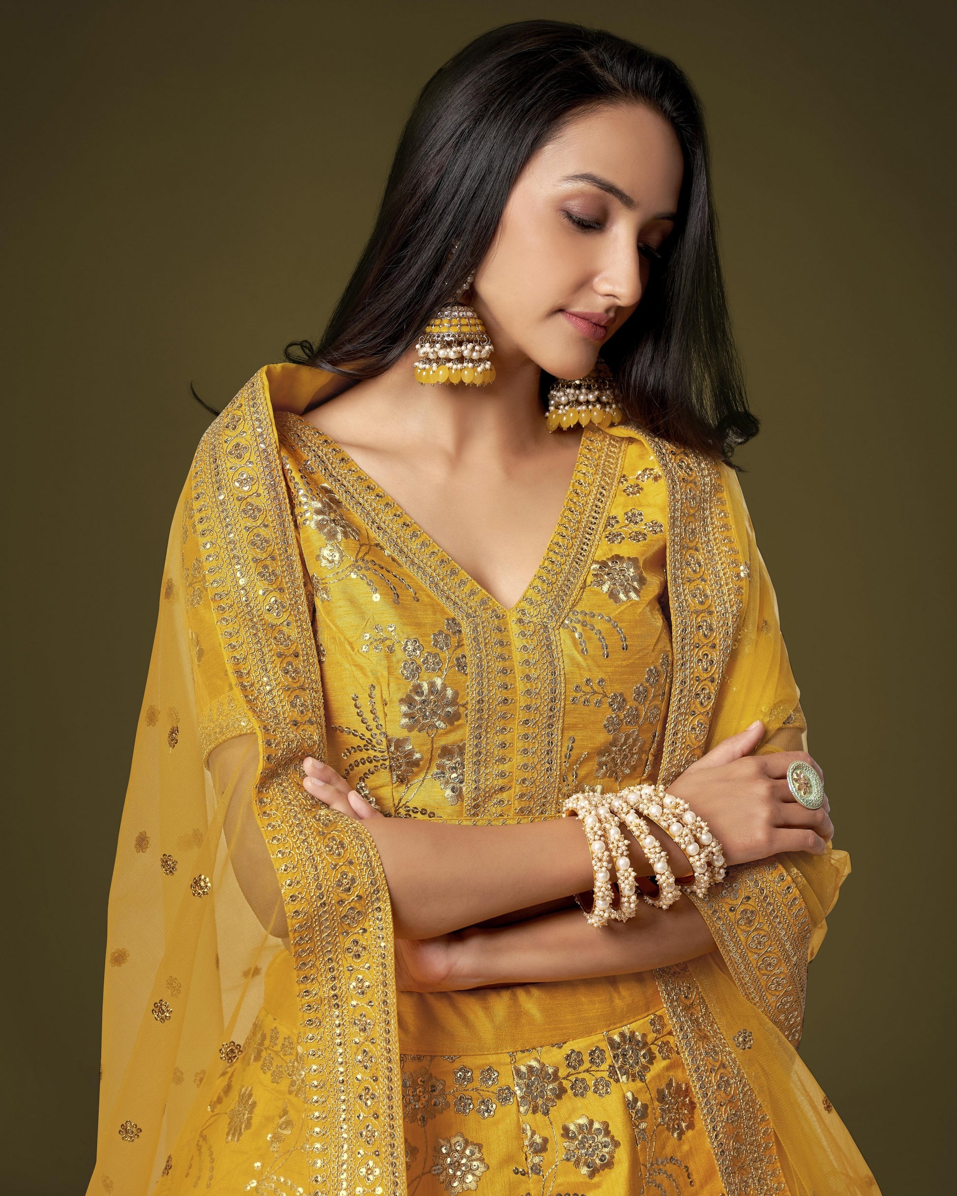 Woman wearing a yellow embroidered traditional outfit with jewelry on a brown background