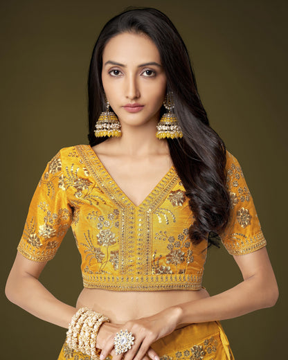 Woman wearing a yellow embroidered blouse with gold jewelry against a brown background