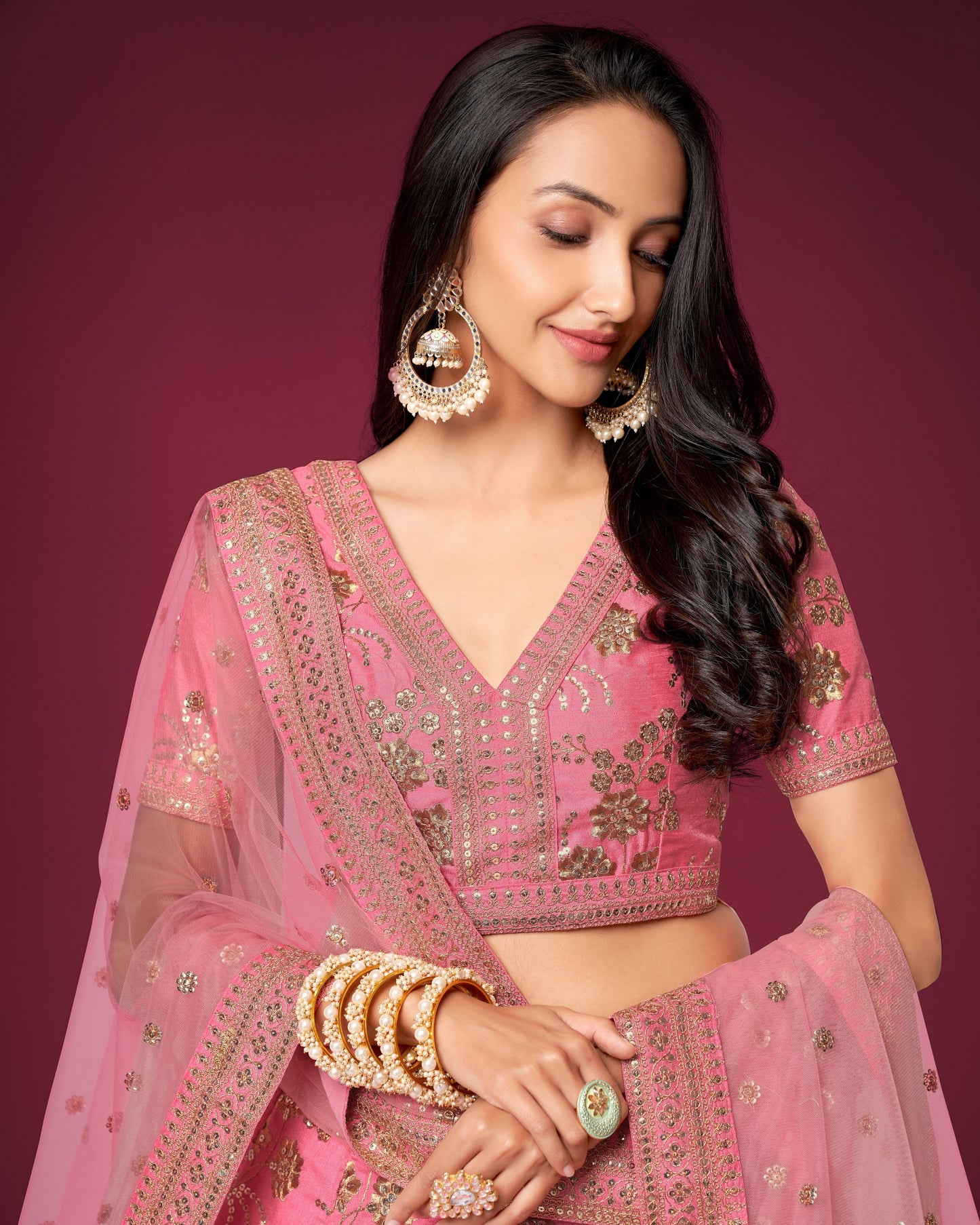 Woman wearing a pink traditional outfit with gold embroidery against a purple background