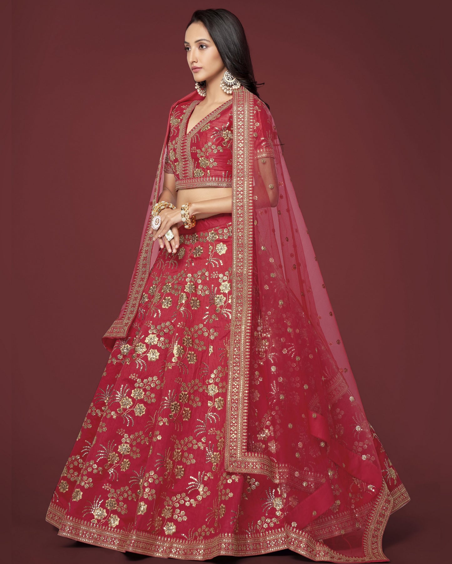 Woman wearing a red embroidered lehenga with gold details on a maroon background