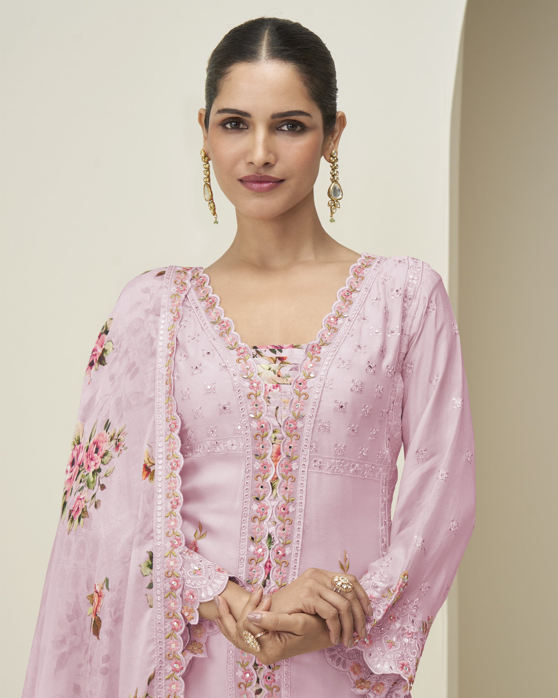 Woman wearing a pink embroidered outfit with a matching dupatta against a plain background