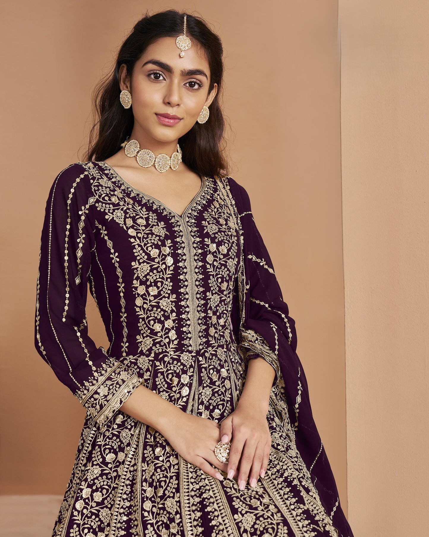 Woman wearing a purple and gold embroidered traditional outfit against a beige background