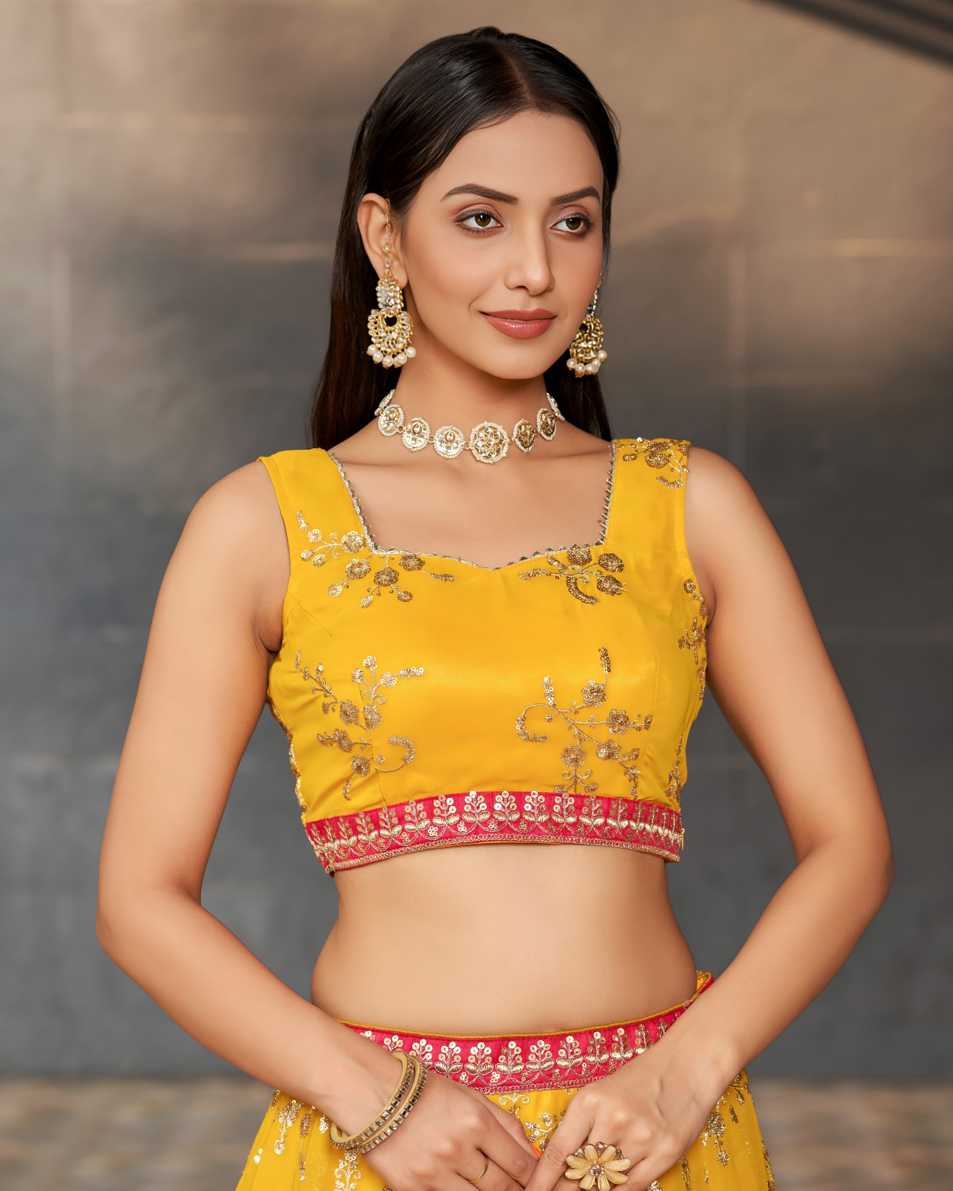 Woman wearing a yellow embroidered blouse with a matching saree against a neutral background