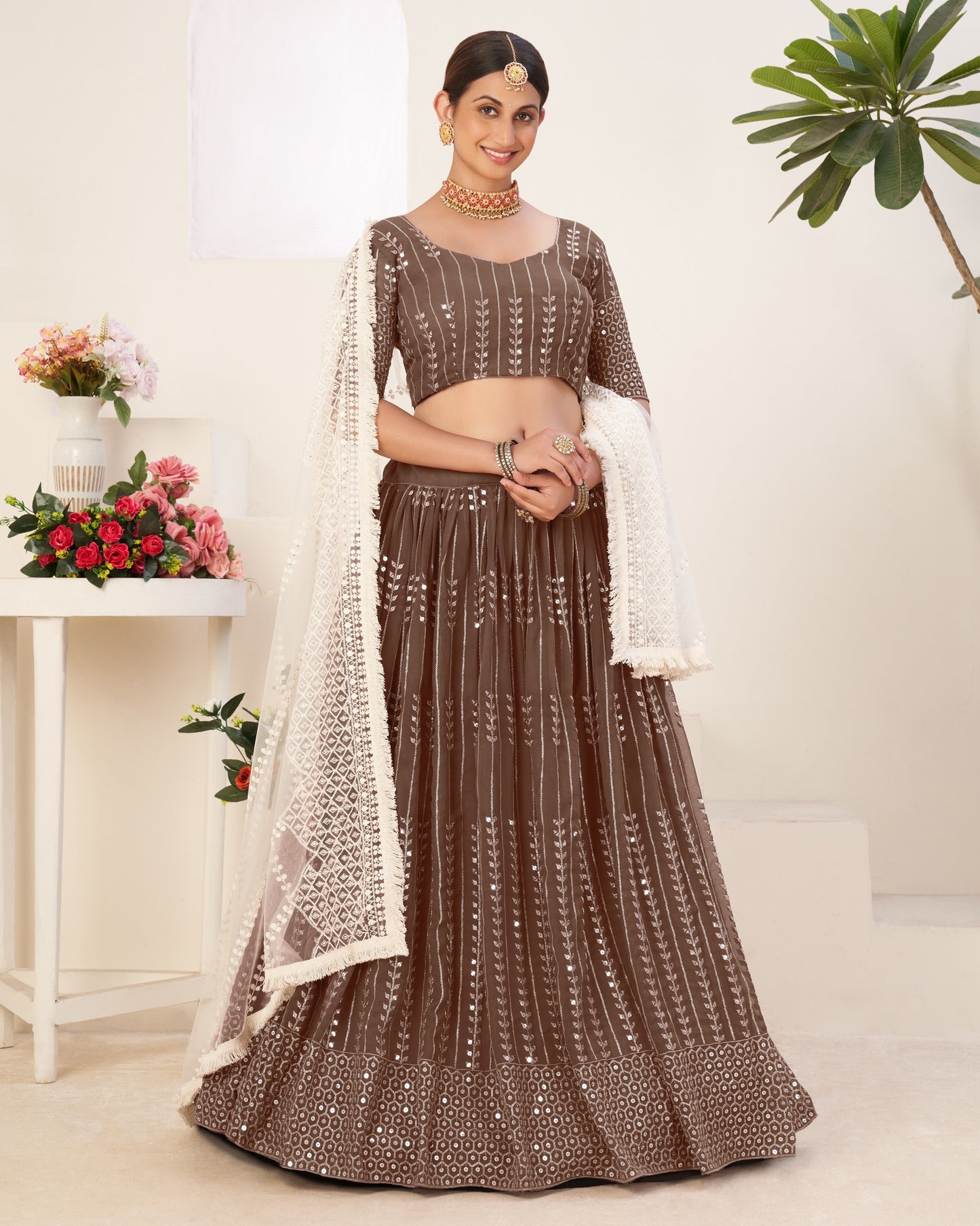 Woman wearing a brown traditional outfit with a white dupatta in a minimalistic setting.