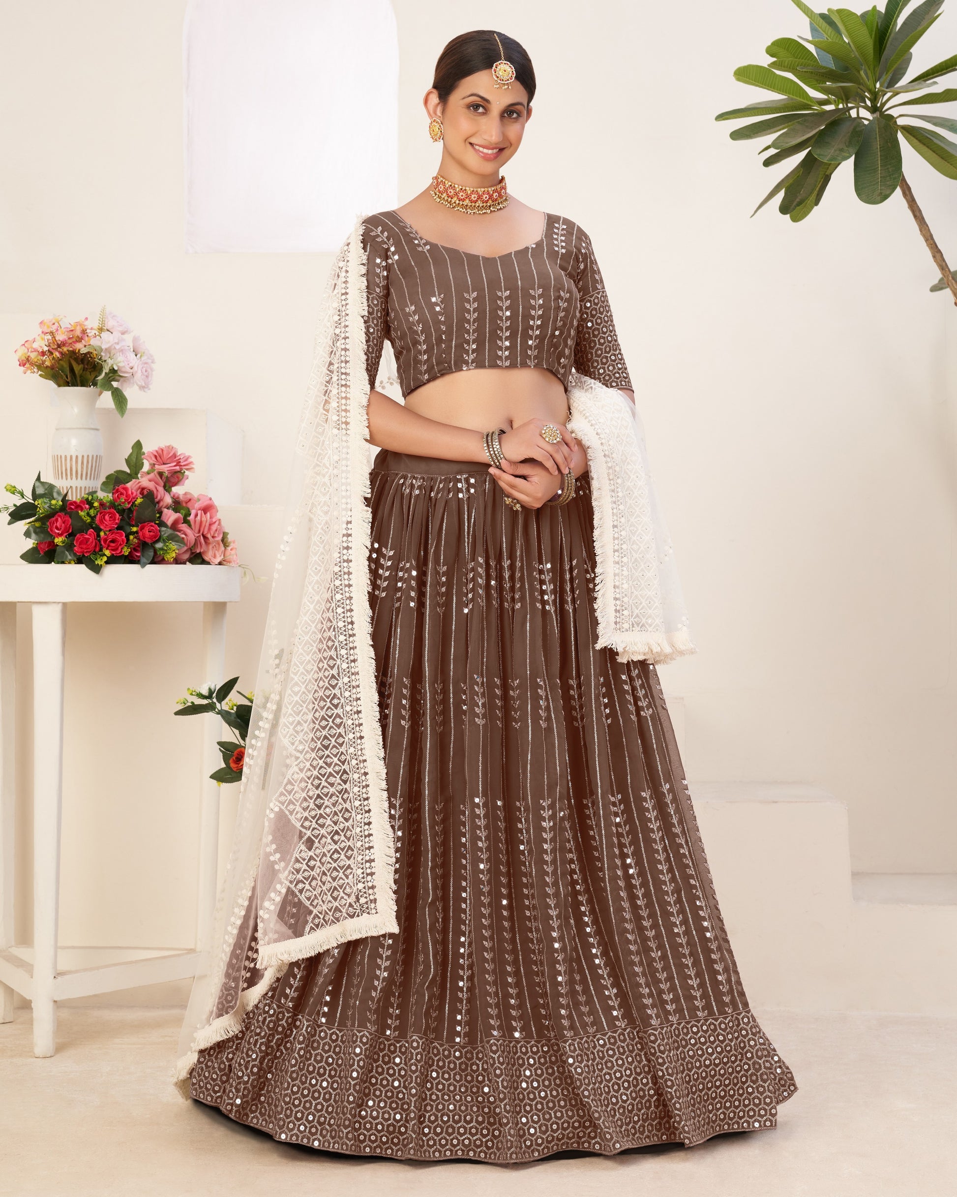 Woman wearing a brown traditional outfit with a white dupatta in a minimalistic setting.