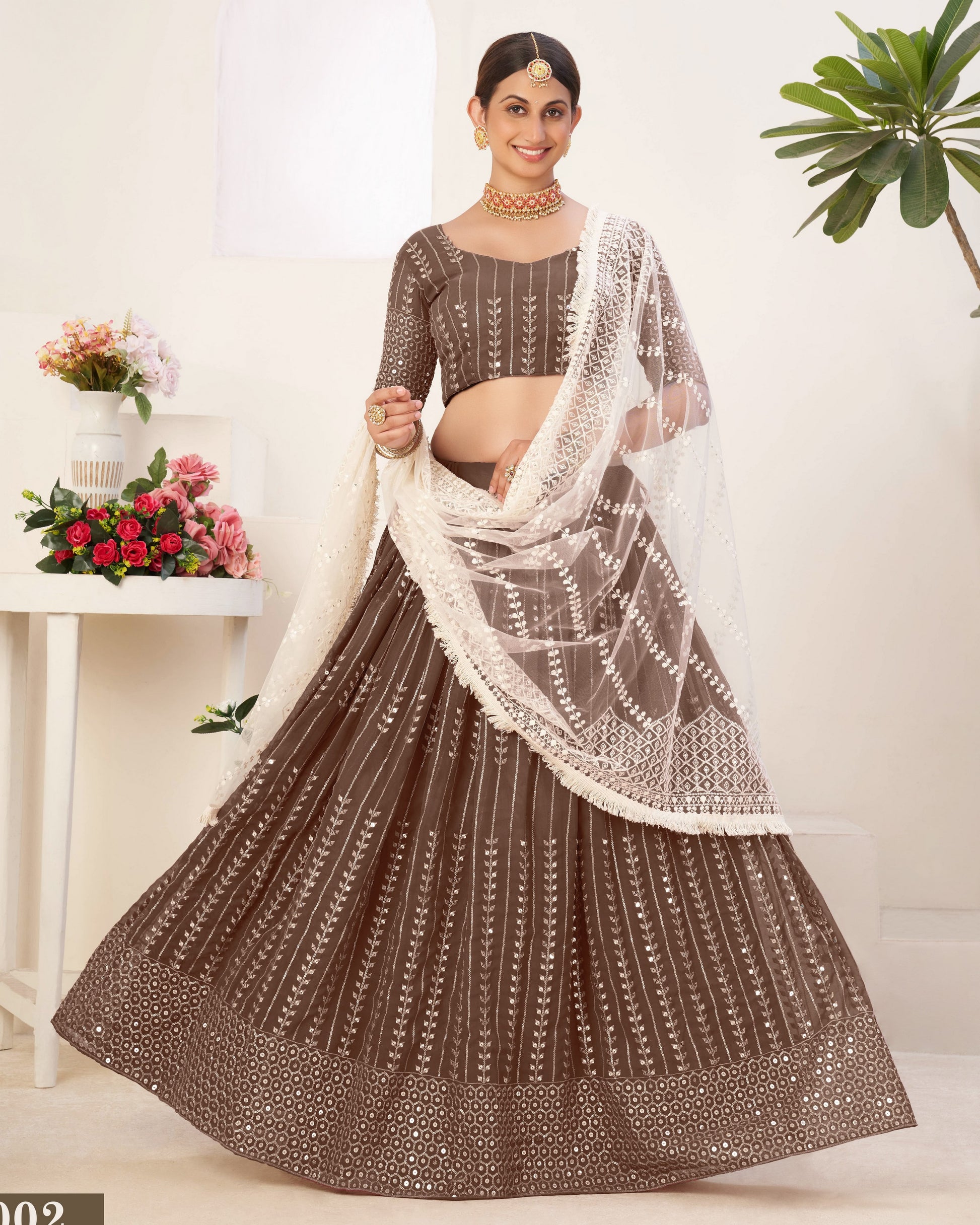 Woman wearing a brown and white traditional outfit with a white dupatta, standing against a white background.