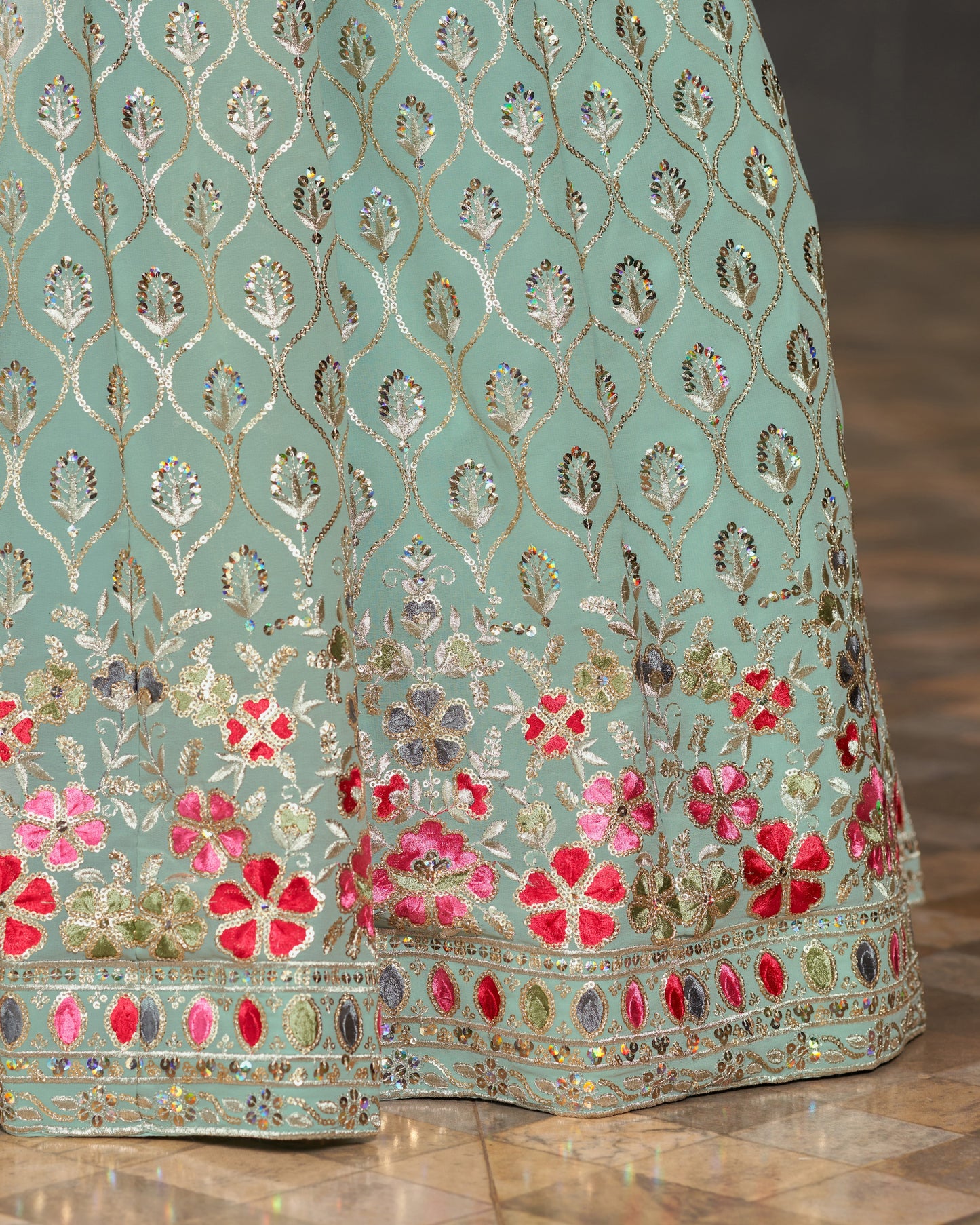 Light blue fabric with floral embroidery and sequins on a wooden floor.