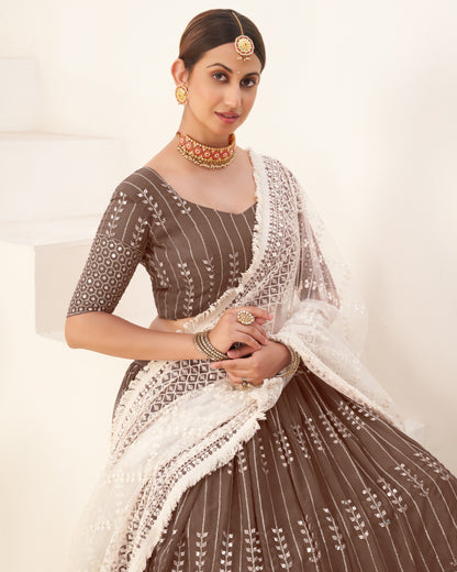 Woman wearing a traditional brown and white embroidered outfit with jewelry on a light background