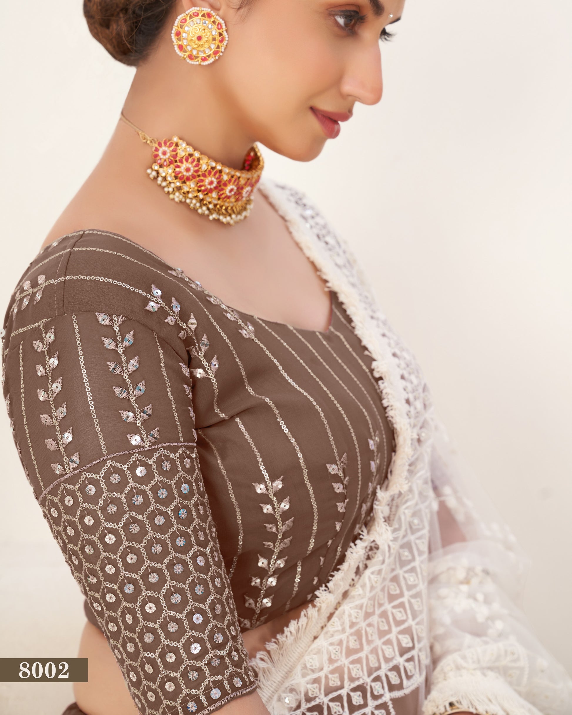 Woman wearing a traditional brown and white saree with gold jewelry on a beige background