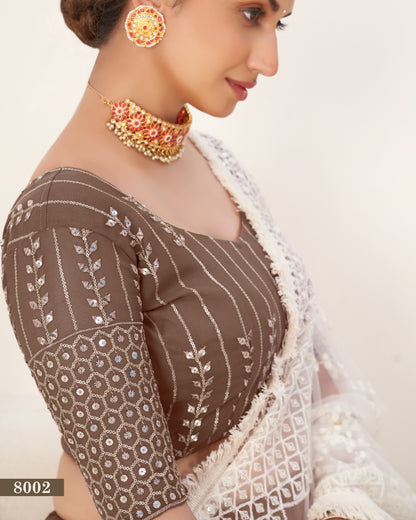 Woman wearing a traditional brown and white saree with gold jewelry on a beige background
