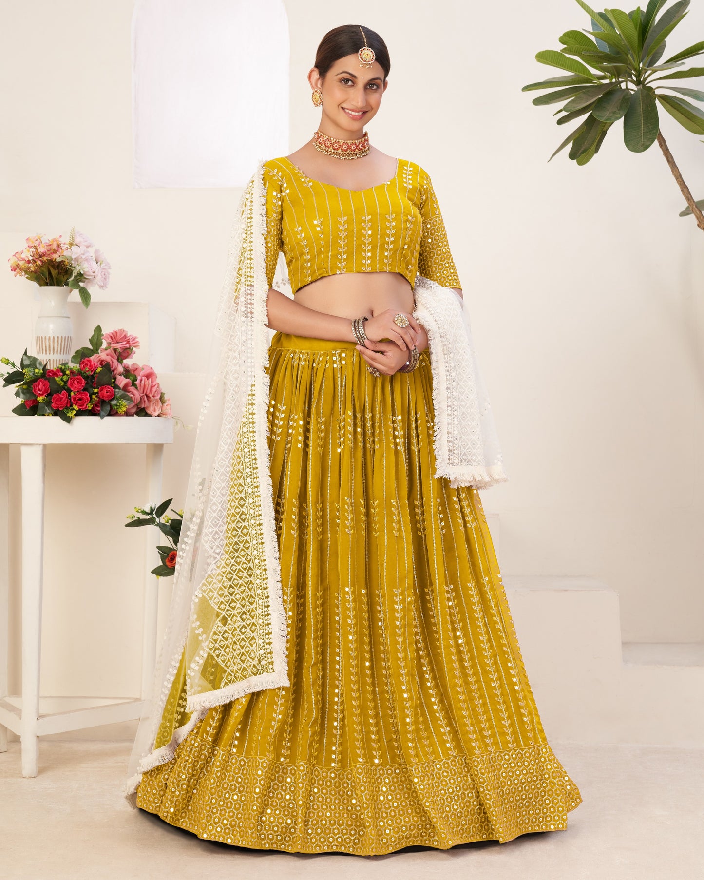 Woman wearing a yellow traditional outfit with a white dupatta in a minimalistic setting.