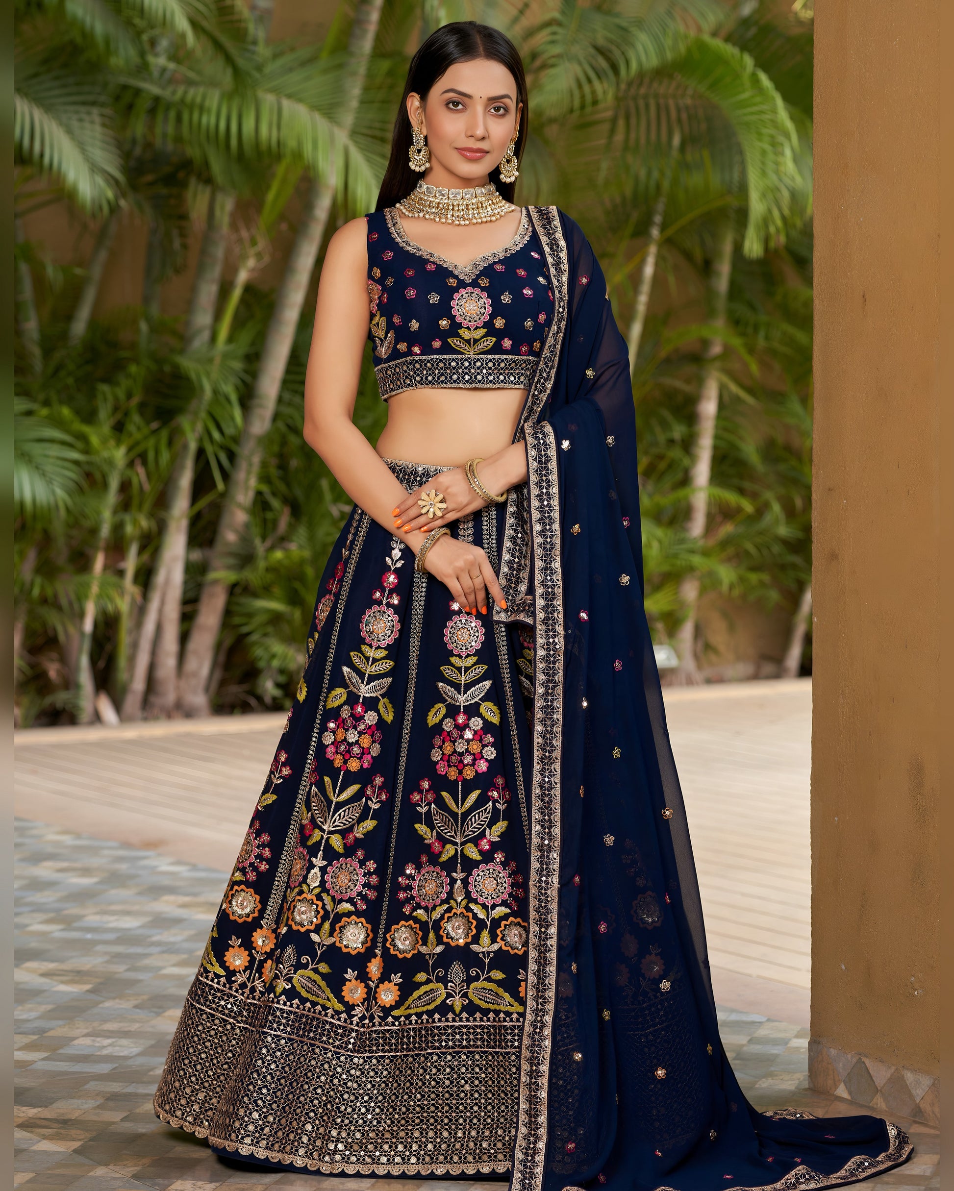 Woman in a traditional navy blue embroidered outfit standing outdoors with greenery in the background