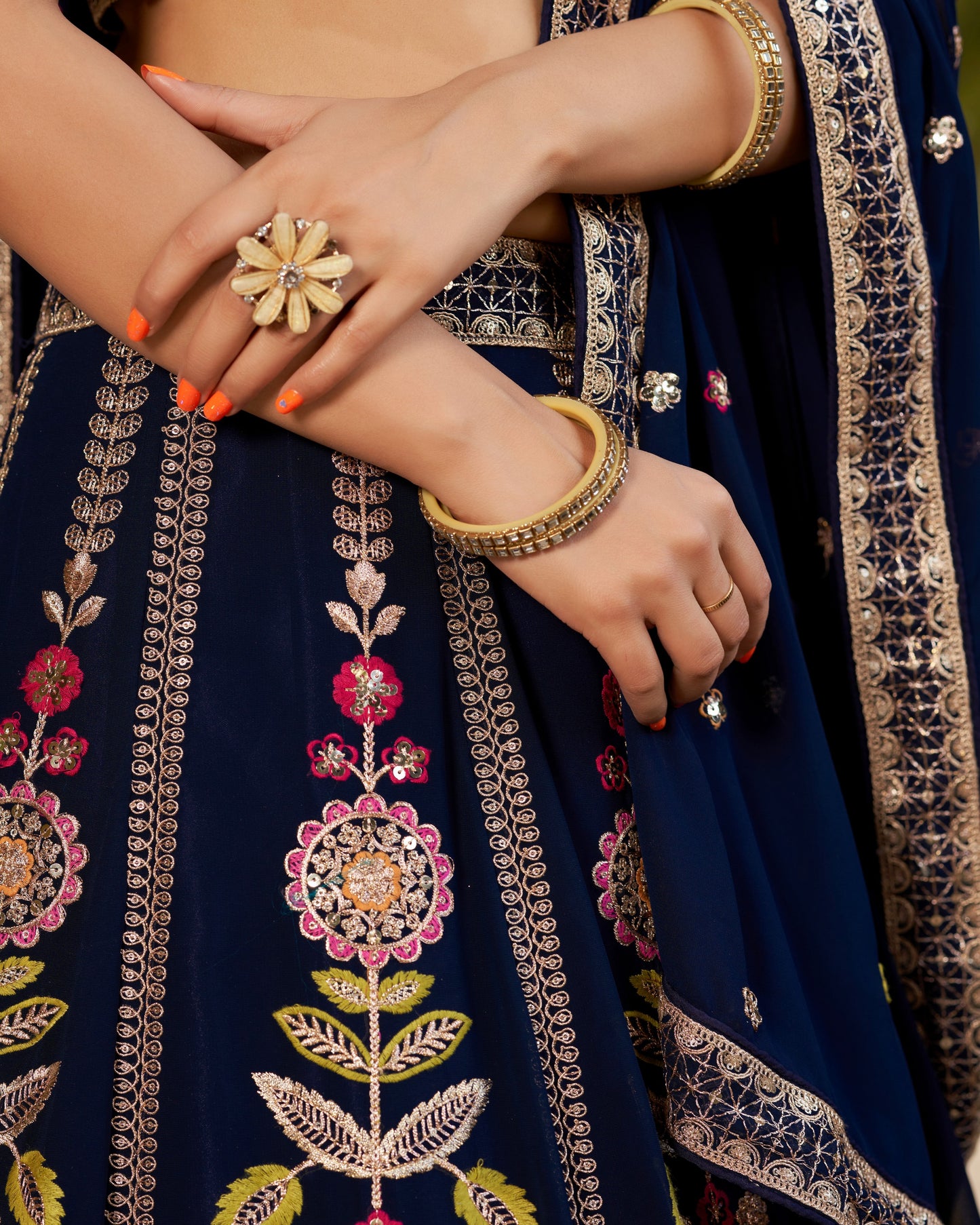 Close-up of a person wearing a navy blue embroidered outfit with gold jewelry.
