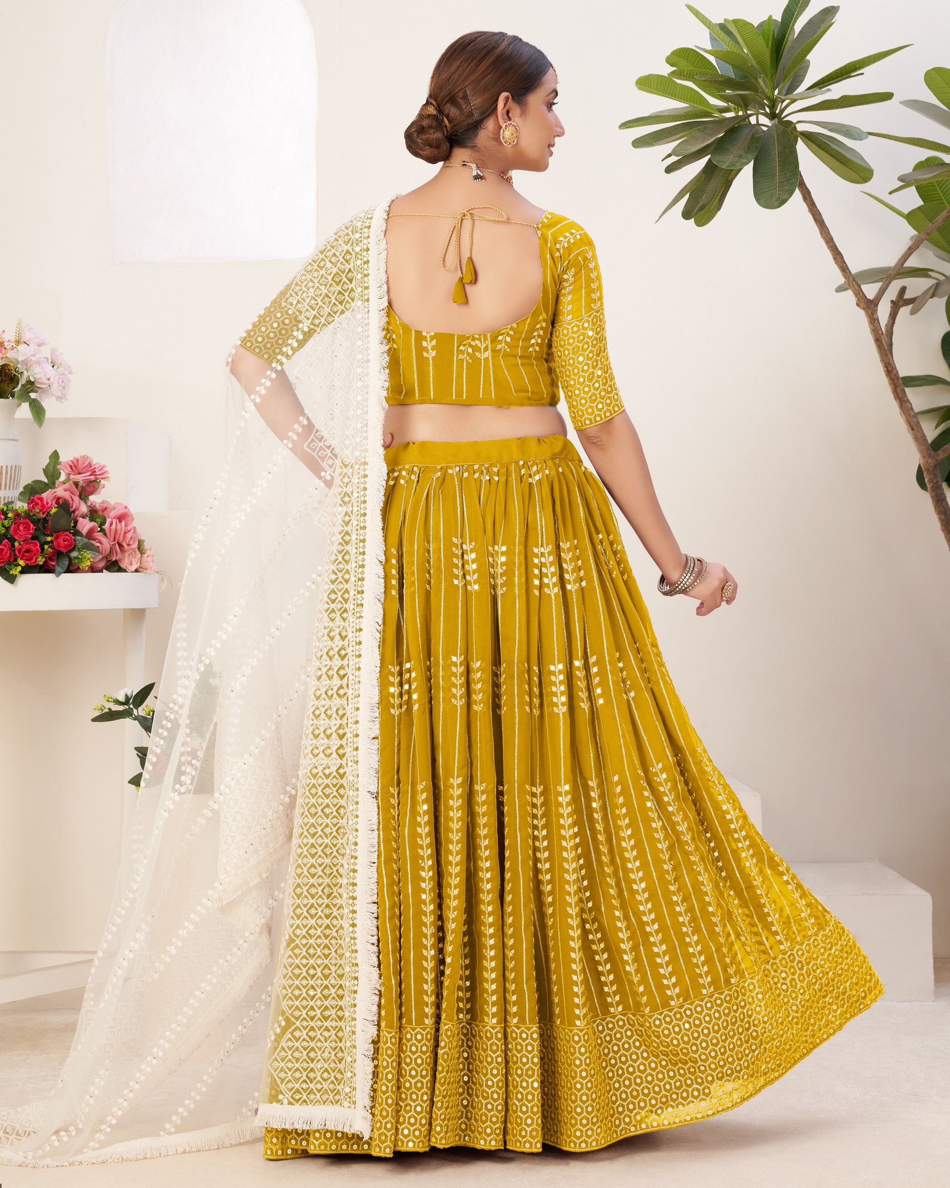 Woman wearing a yellow embroidered traditional outfit with a white dupatta in a minimalistic setting.