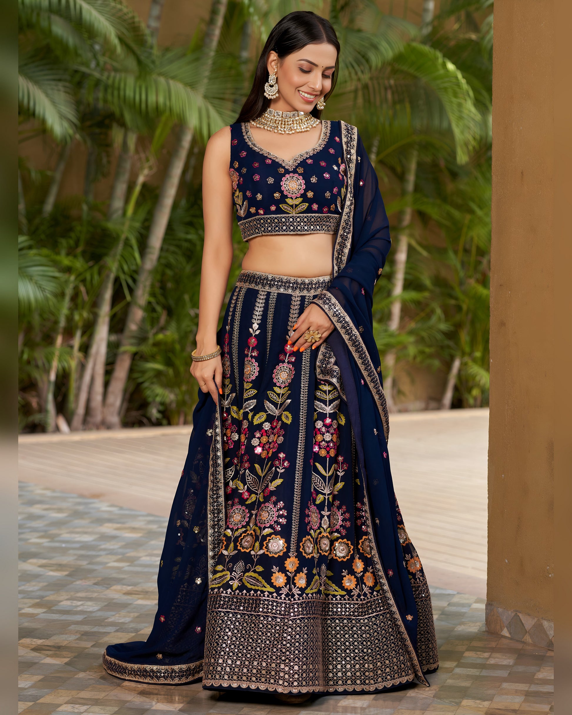 Woman wearing a traditional embroidered navy blue lehenga with a green outdoor background