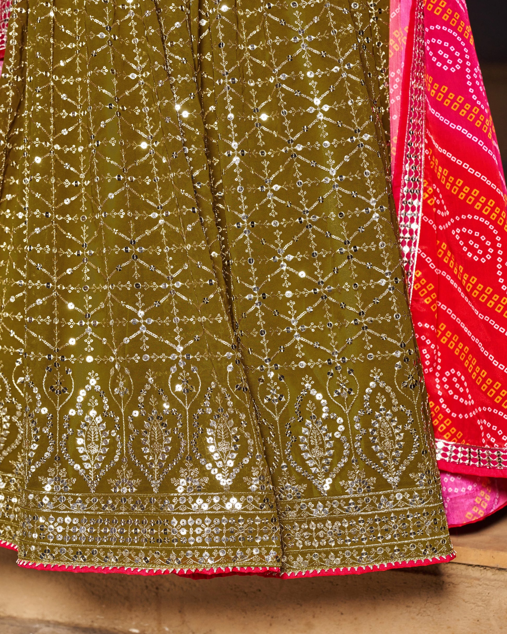 Close-up of a green embroidered fabric with silver detailing and a pink border.