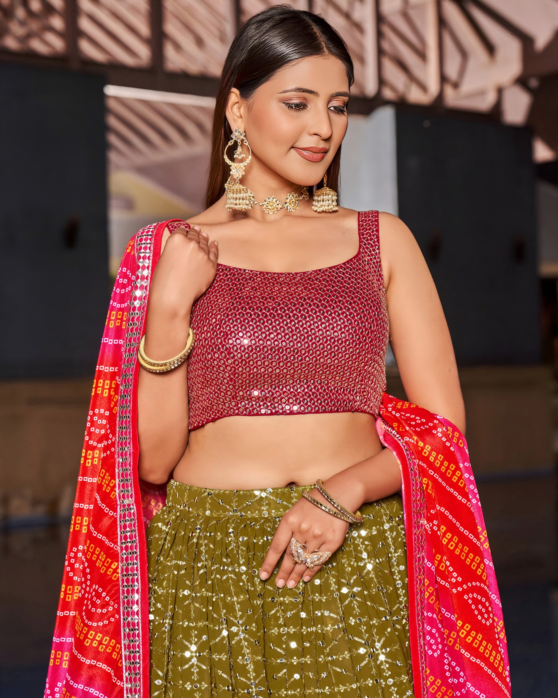 Woman wearing a red blouse and green skirt with a red dupatta, standing against a blurred background.