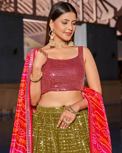 Woman wearing a red blouse and green skirt with a red dupatta, standing against a blurred background.