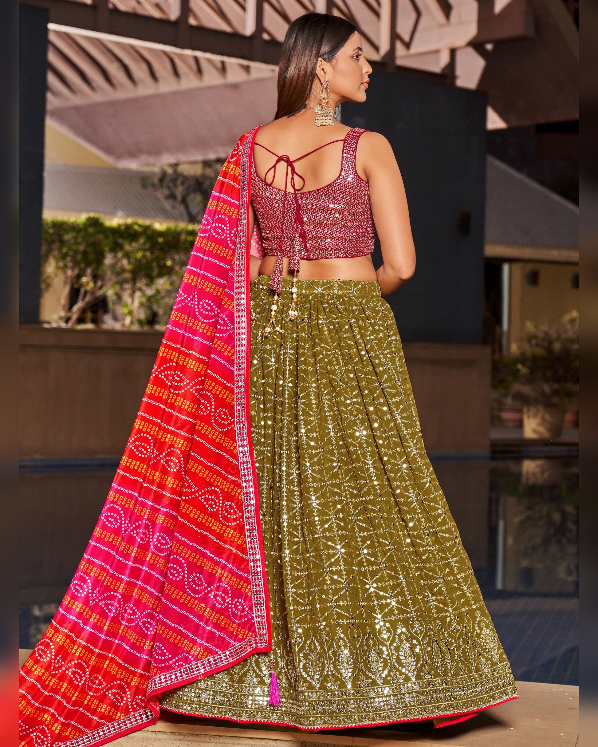 Woman wearing a traditional outfit with a red dupatta and green lehenga in an outdoor setting.