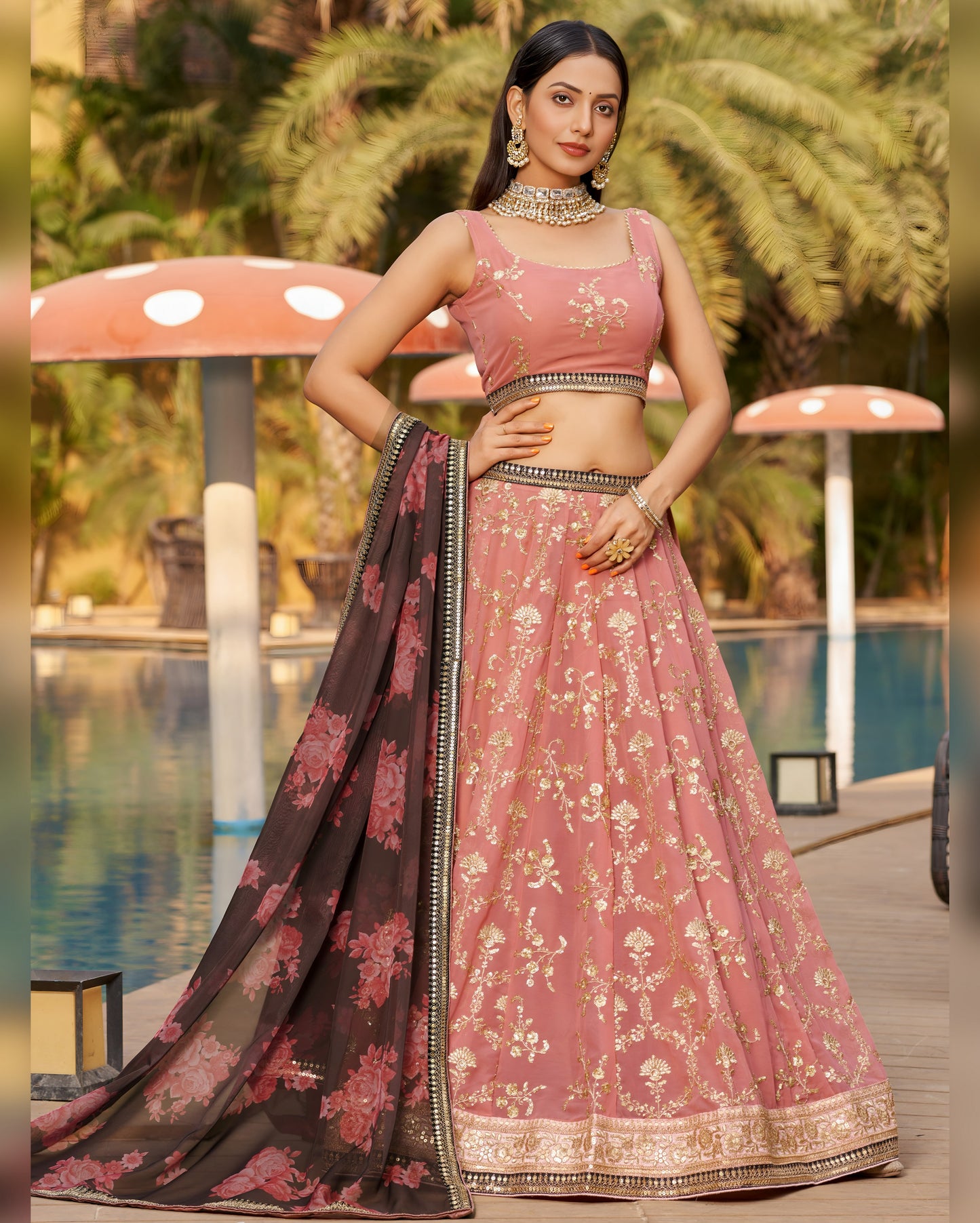 Woman in a traditional pink and black embroidered lehenga by a poolside.