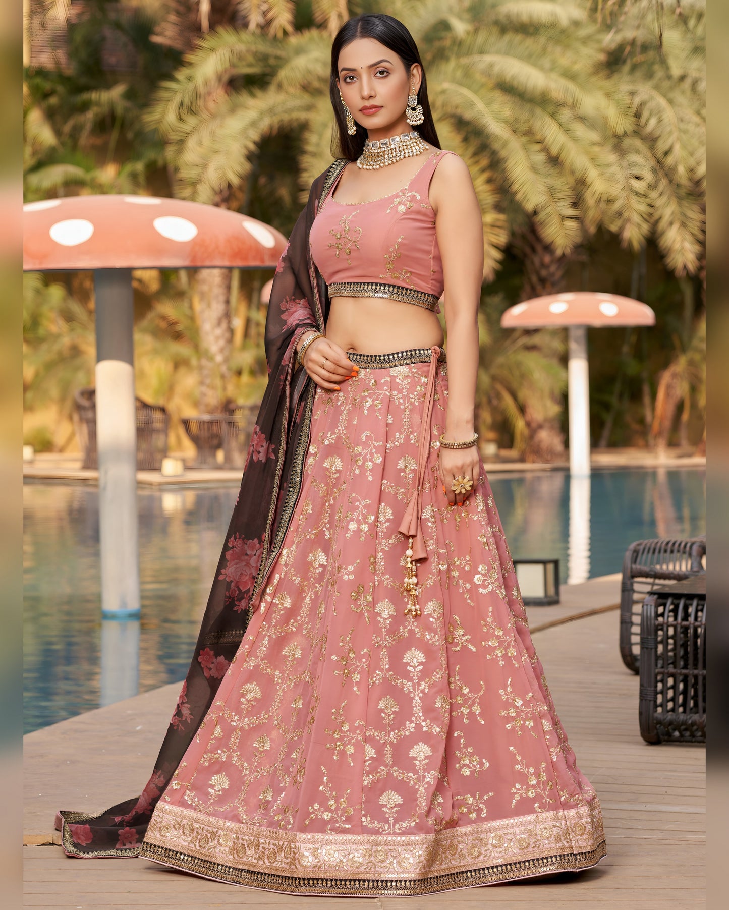Woman in a traditional pink and black lehenga by a poolside