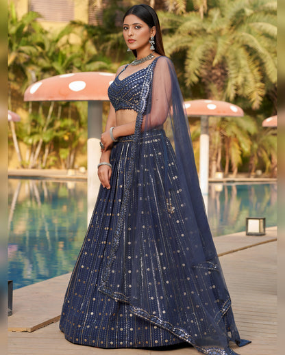 Woman in a blue traditional outfit standing by a pool with greenery in the background