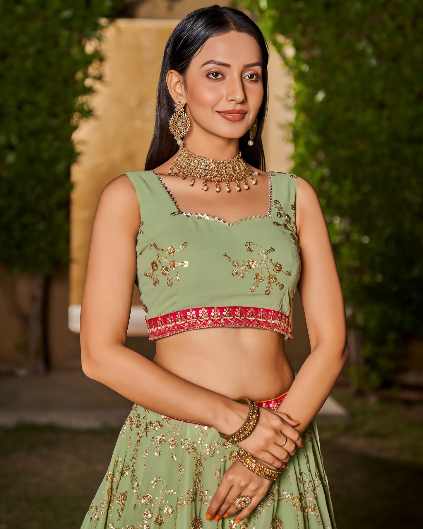Woman wearing a green embroidered traditional outfit with jewelry against a blurred natural background
