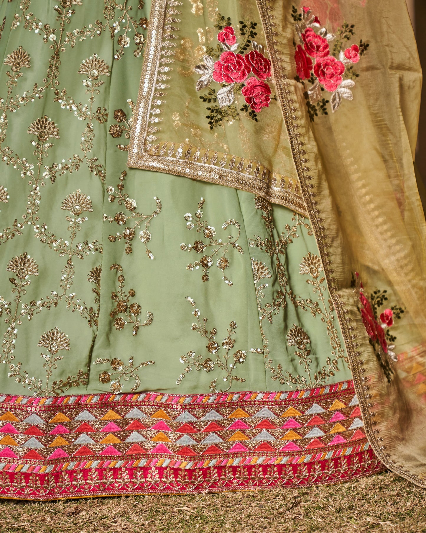Close-up of a green embroidered fabric with floral patterns and red flowers.
