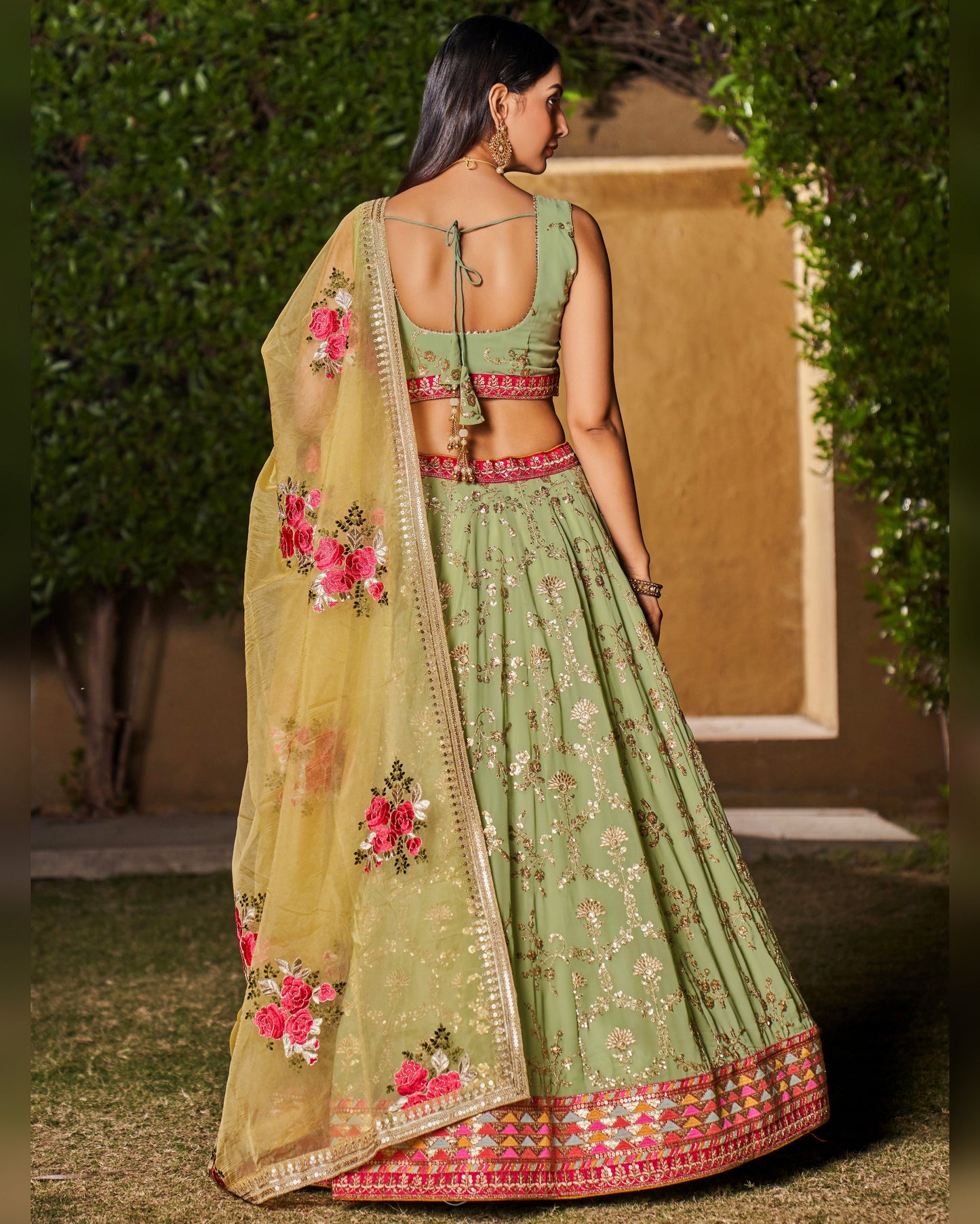 Woman wearing a green embroidered lehenga with a floral dupatta in an outdoor setting.