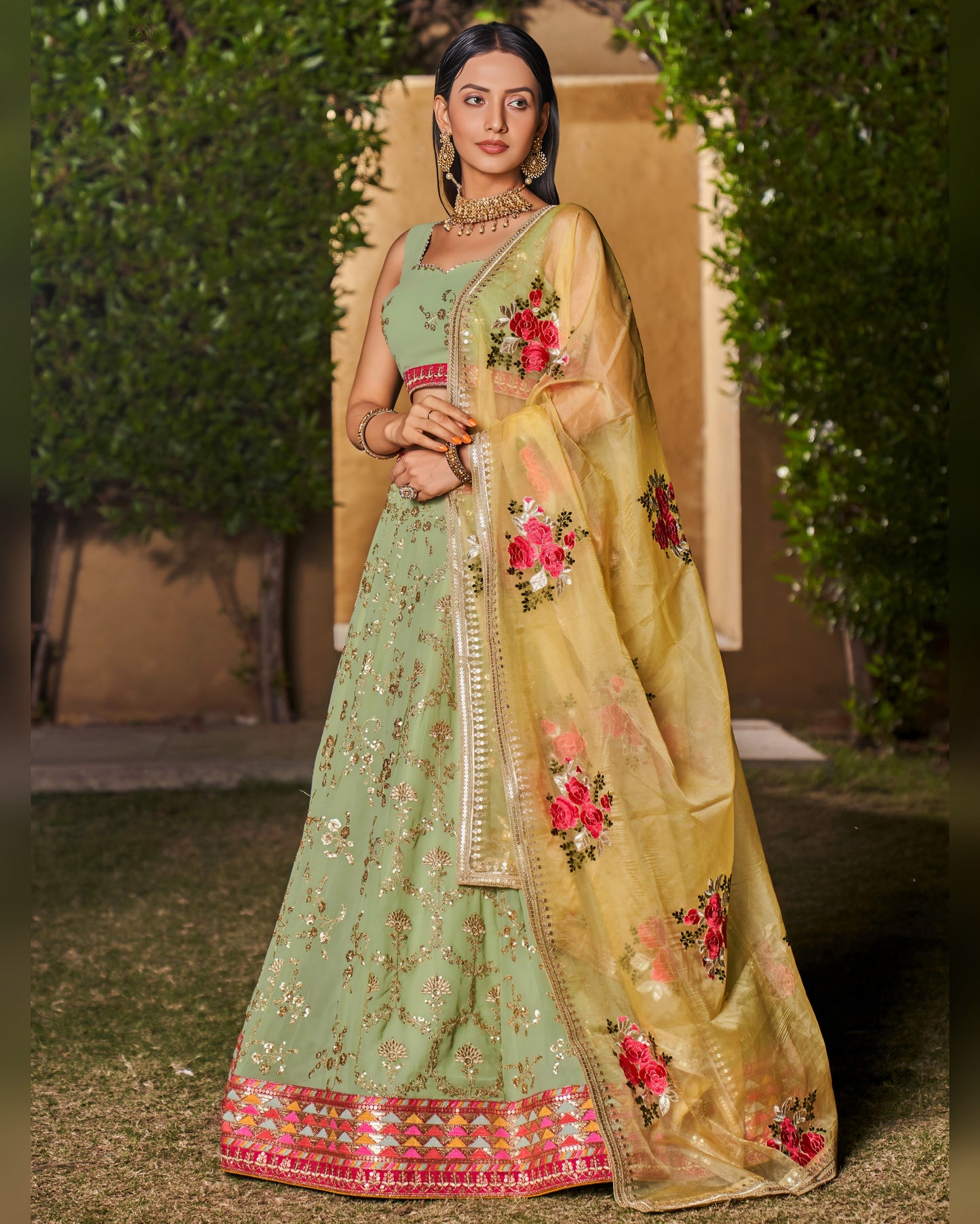 Woman wearing a traditional green and beige embroidered saree with a floral design.
