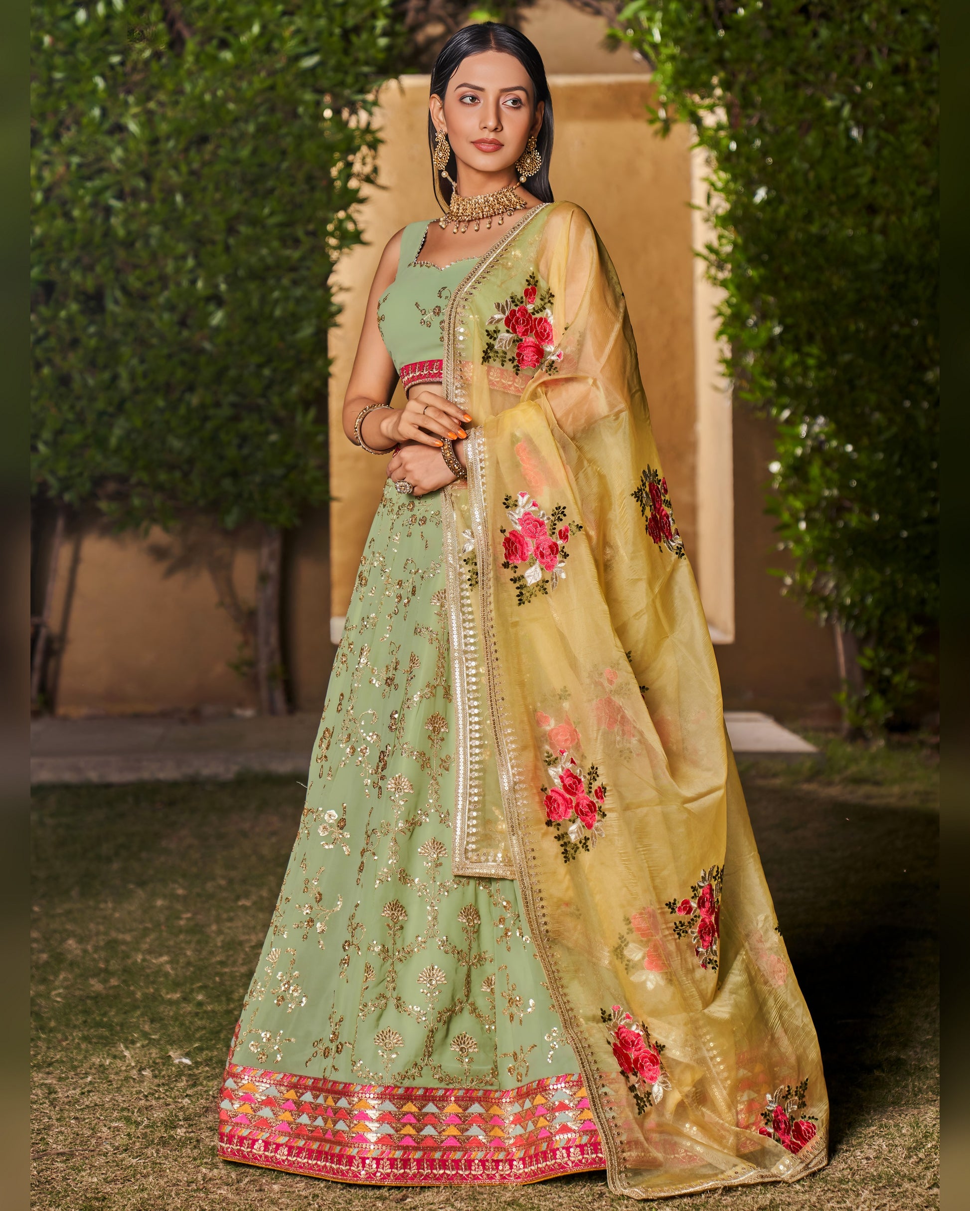 Woman wearing a traditional green and beige embroidered saree with a floral design.