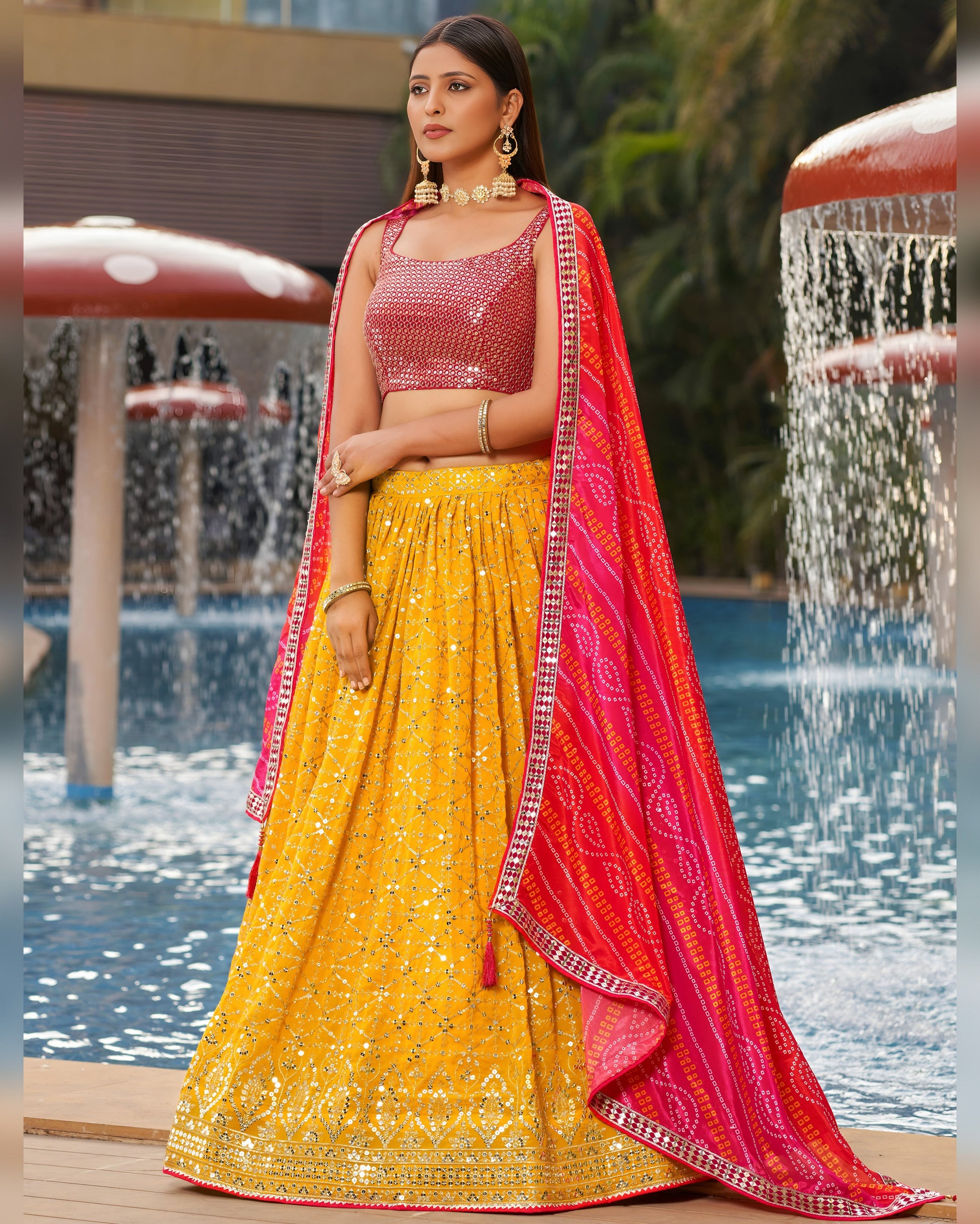 Woman in a yellow and pink traditional outfit standing by a pool with water features.